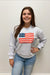 Person wearing a light blue sweatshirt with an American flag design against a plain background