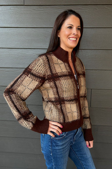 Woman wearing Z Supply Frostline Plaid Cardigan In Toasted Almond with blue jeans on a dark wood background.