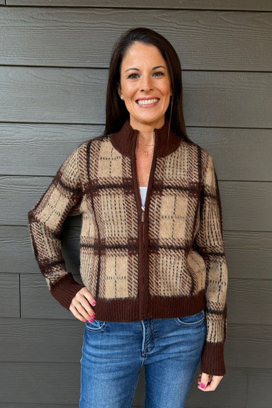 Woman wearing Z Supply Frostline Plaid Cardigan In Toasted Almond with blue jeans on a dark wood background.