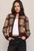 A woman modeling a brown and beige plaid knit cardigan with a mock neck and ribbed cuffs, worn over a white crop top and black jeans against a solid light beige background.