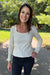 A woman smiling outdoors on a paved path wearing a fitted long-sleeve scoop-neck top in a light cream color, paired with black pants.