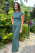 A woman wearing a matching sage green two-piece lounge set consisting of a short-sleeve crewneck top and wide-leg pants, standing on a stone pathway in a lush garden setting.