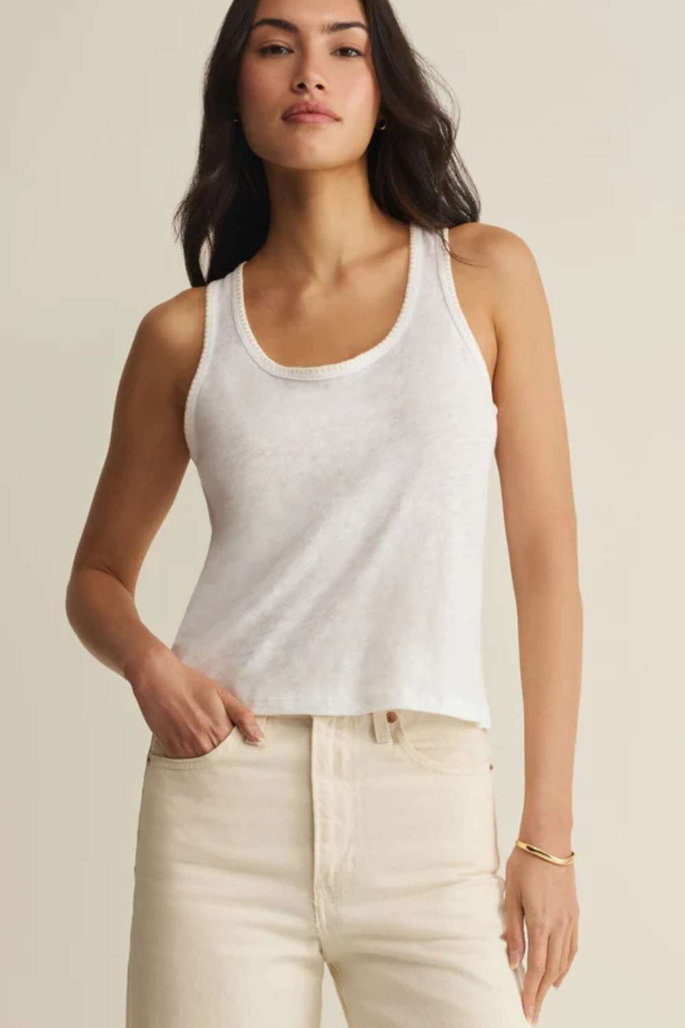 Woman wearing a white tank top and beige pants against a plain background