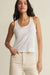 Woman wearing a white tank top and beige pants against a plain background