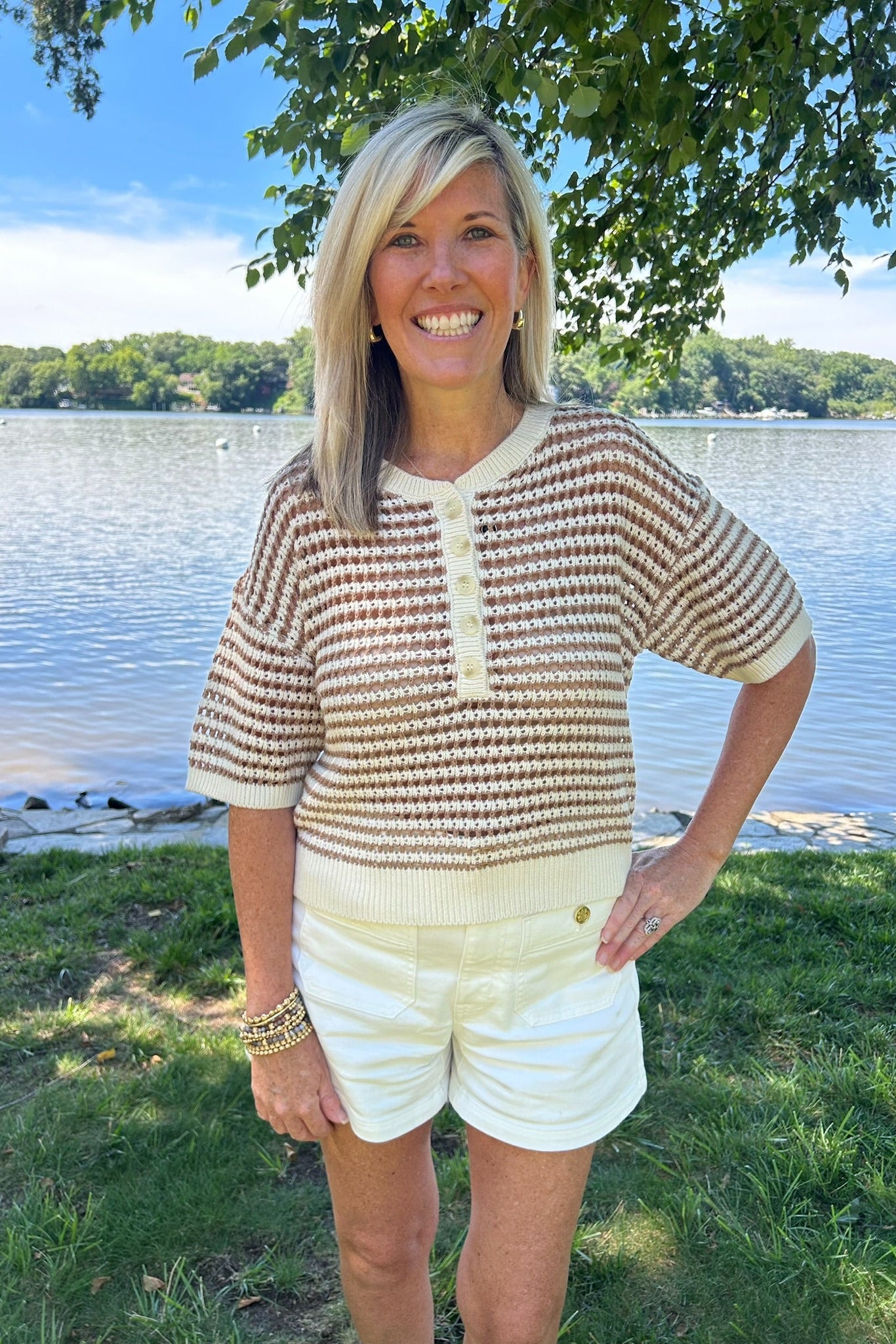 Woman standing by a lake wearing a patterned shirt and white shorts.