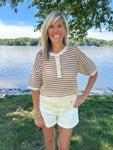 Woman standing by a lake wearing a patterned shirt and white shorts.