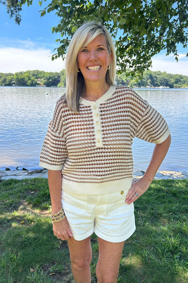 Woman standing by a lake wearing a patterned shirt and white shorts.