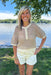 Woman standing by a lake wearing a patterned shirt and white shorts.