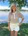 Woman standing by a lake wearing a patterned shirt and white shorts.