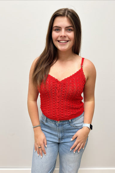 Woman wearing a red lace top and blue jeans against a plain background