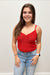 Woman wearing a red lace top and blue jeans against a plain background