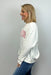 Woman wearing a white sweatshirt with red text and blue jeans against a plain background