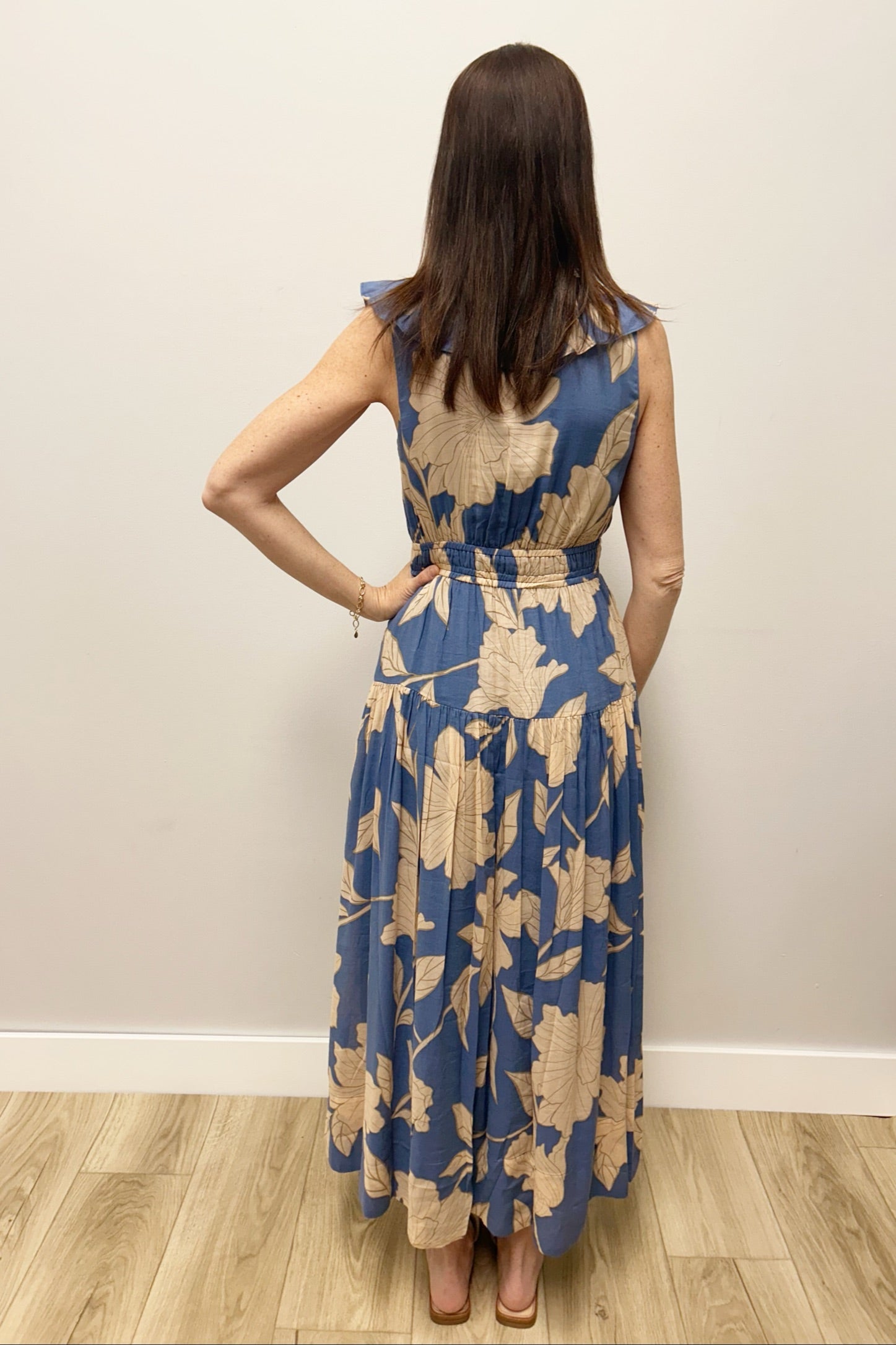 Woman wearing a blue floral dress standing against a plain wall.