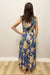 Woman wearing a blue floral dress standing against a plain wall.