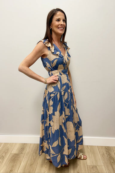 Woman wearing a blue floral dress standing against a plain wall.