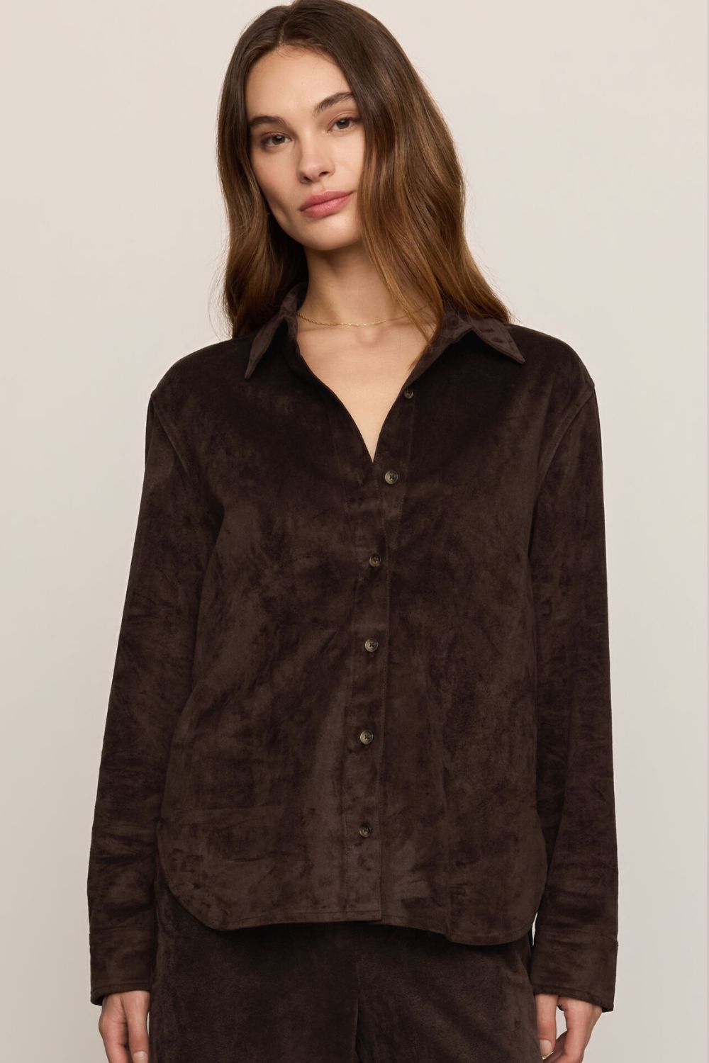 A woman wearing a dark brown long-sleeve button-up shirt made of a textured, velour-like fabric, paired with matching dark brown pants, against a plain light beige background.