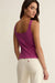 Woman wearing a purple tank top and white pants on a beige background