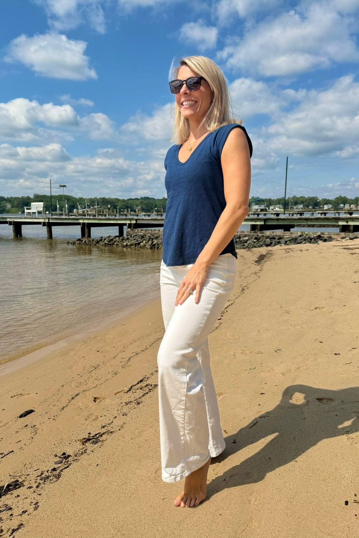 Woman standing on a sandy beach with a blue sky and clouds in the background