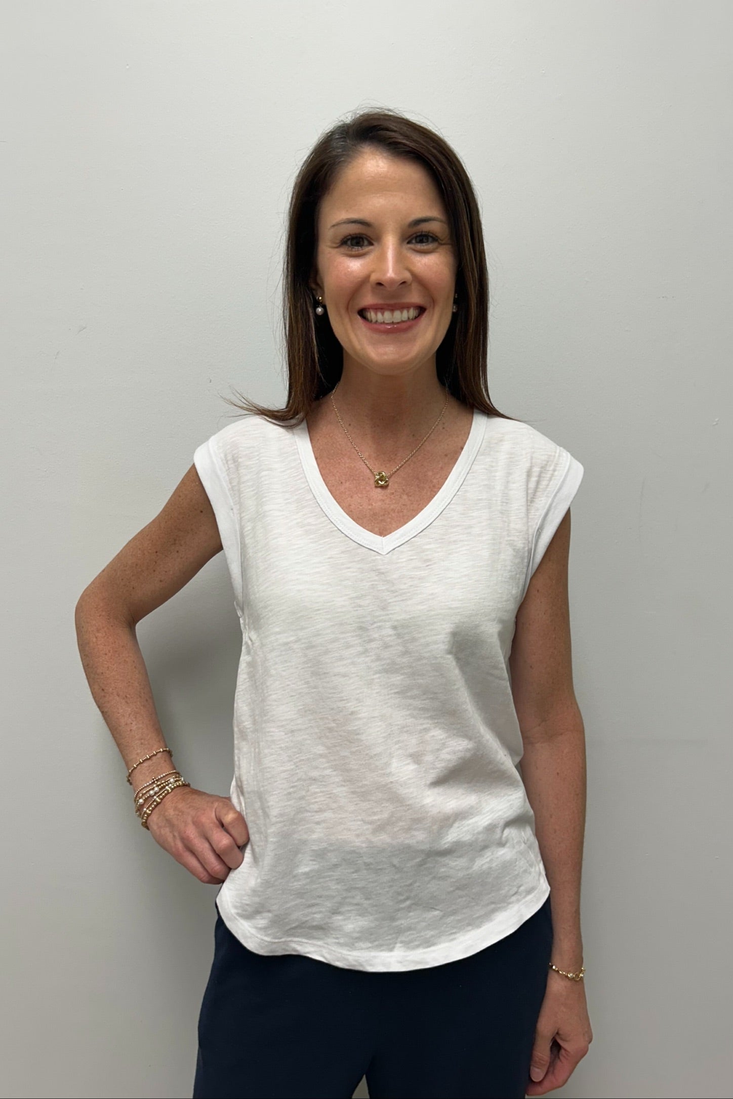 Woman wearing a white t-shirt and dark pants against a plain background