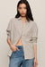 A woman modeling a beige and brown checkered button-down shirt with a twisted front detail, paired with blue jeans, against a solid light beige background.