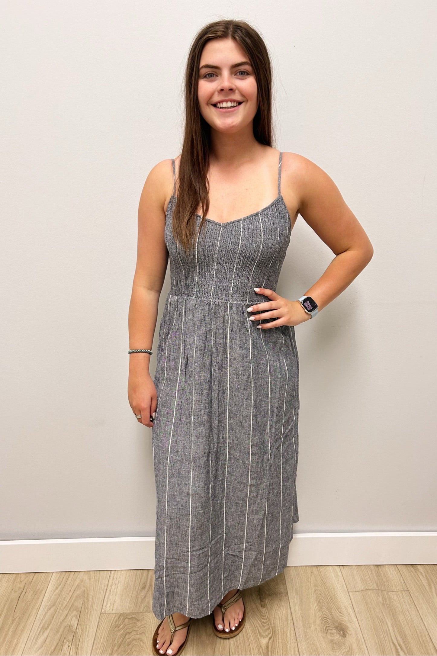 Woman wearing a gray striped dress standing against a plain wall.