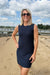 Woman in a navy dress standing on a sandy beach with a blue sky and clouds in the background.