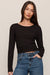 A woman modeling a black long-sleeve crewneck top paired with blue jeans, photographed against a plain light beige studio background.