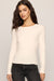 A woman modeling a fitted, long-sleeve crewneck top in a warm off-white or cream color, paired with dark gray jeans, against a solid light gray studio background.
