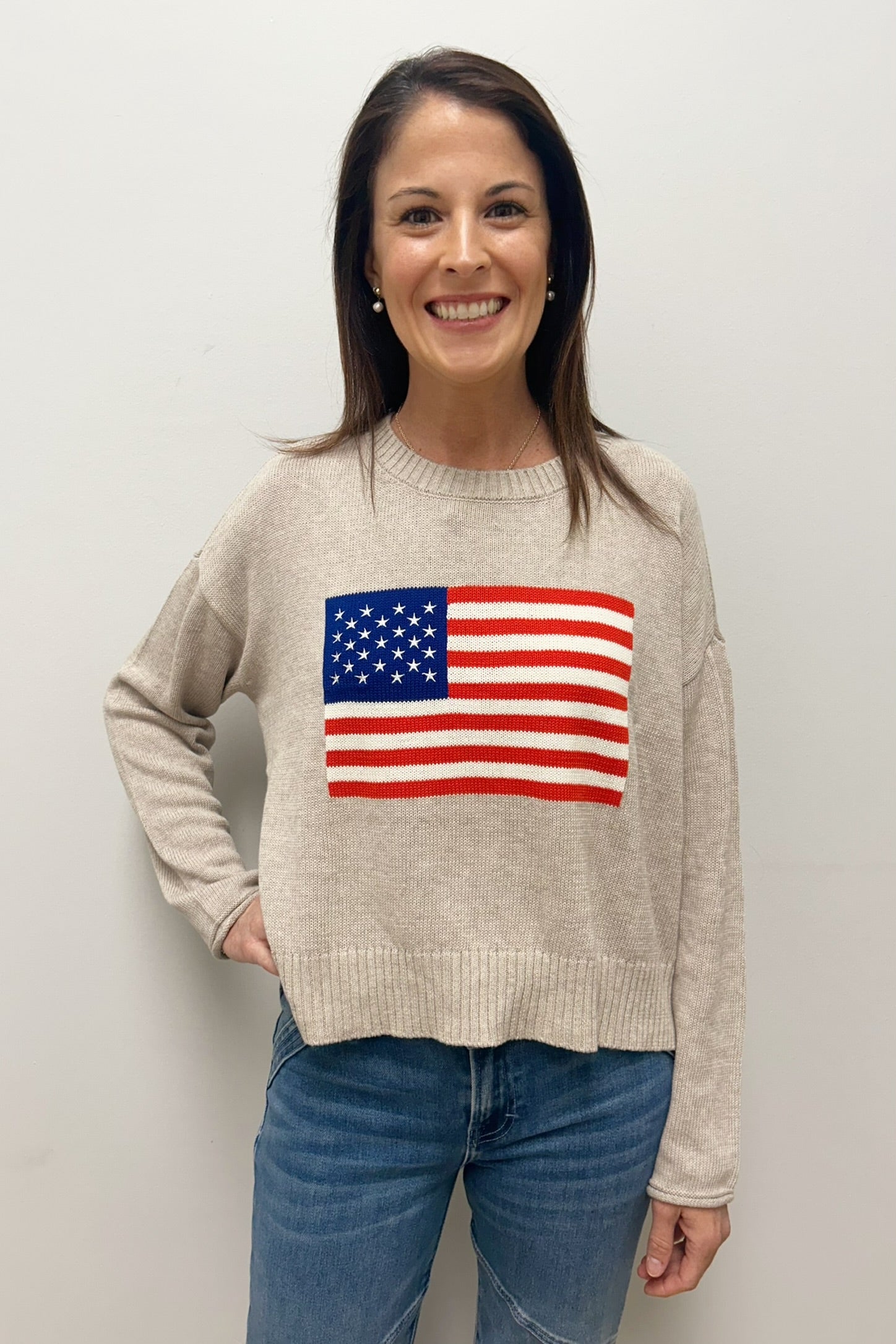 Woman wearing a beige sweater with an American flag design against a plain background