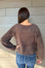 A person shown from the back wearing a fuzzy brown long-sleeve sweater and blue jeans, standing against a light gray wood-paneled wall.