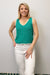 Woman wearing a green sleeveless top and white pants against a plain background