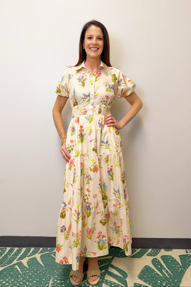Woman wearing a floral dress standing against a plain wall.