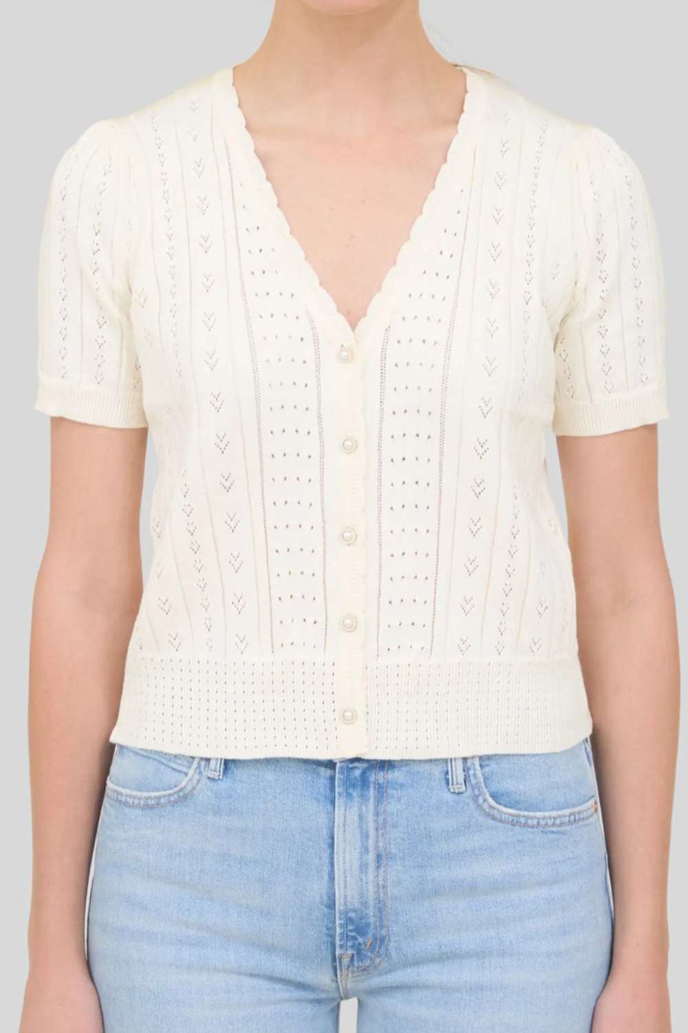 Person wearing a white knitted top and light blue jeans on a plain background