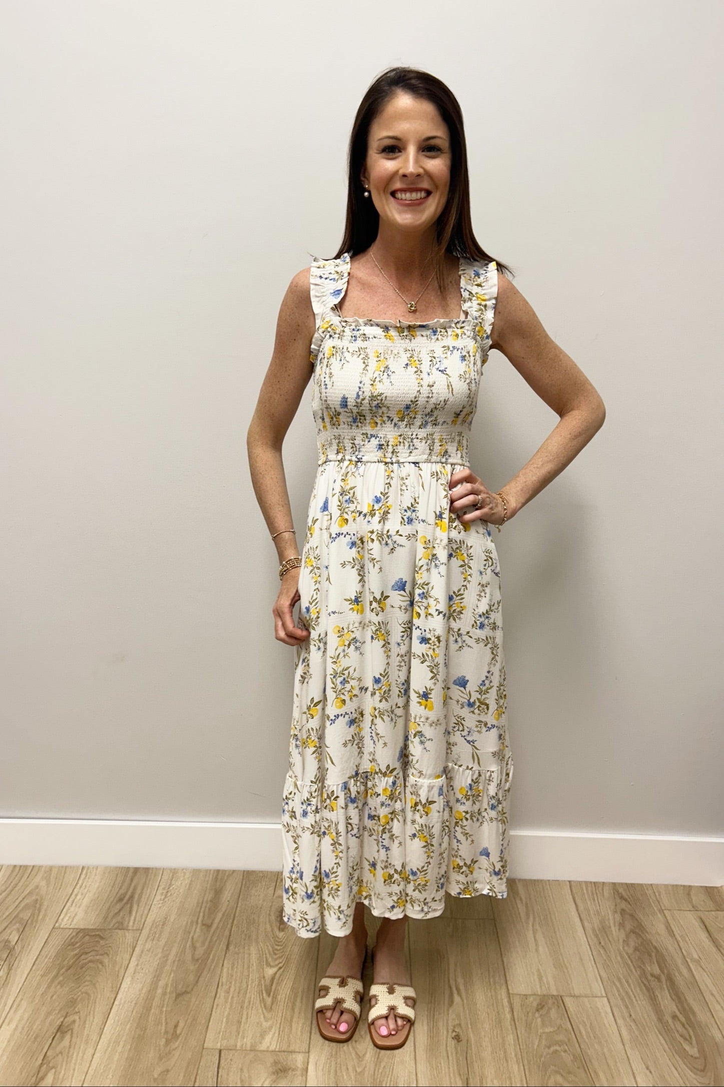 Woman wearing a floral dress standing against a plain wall.