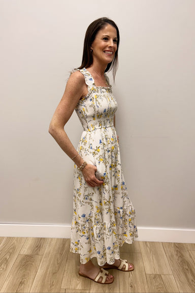 Woman wearing a floral dress standing against a plain wall.