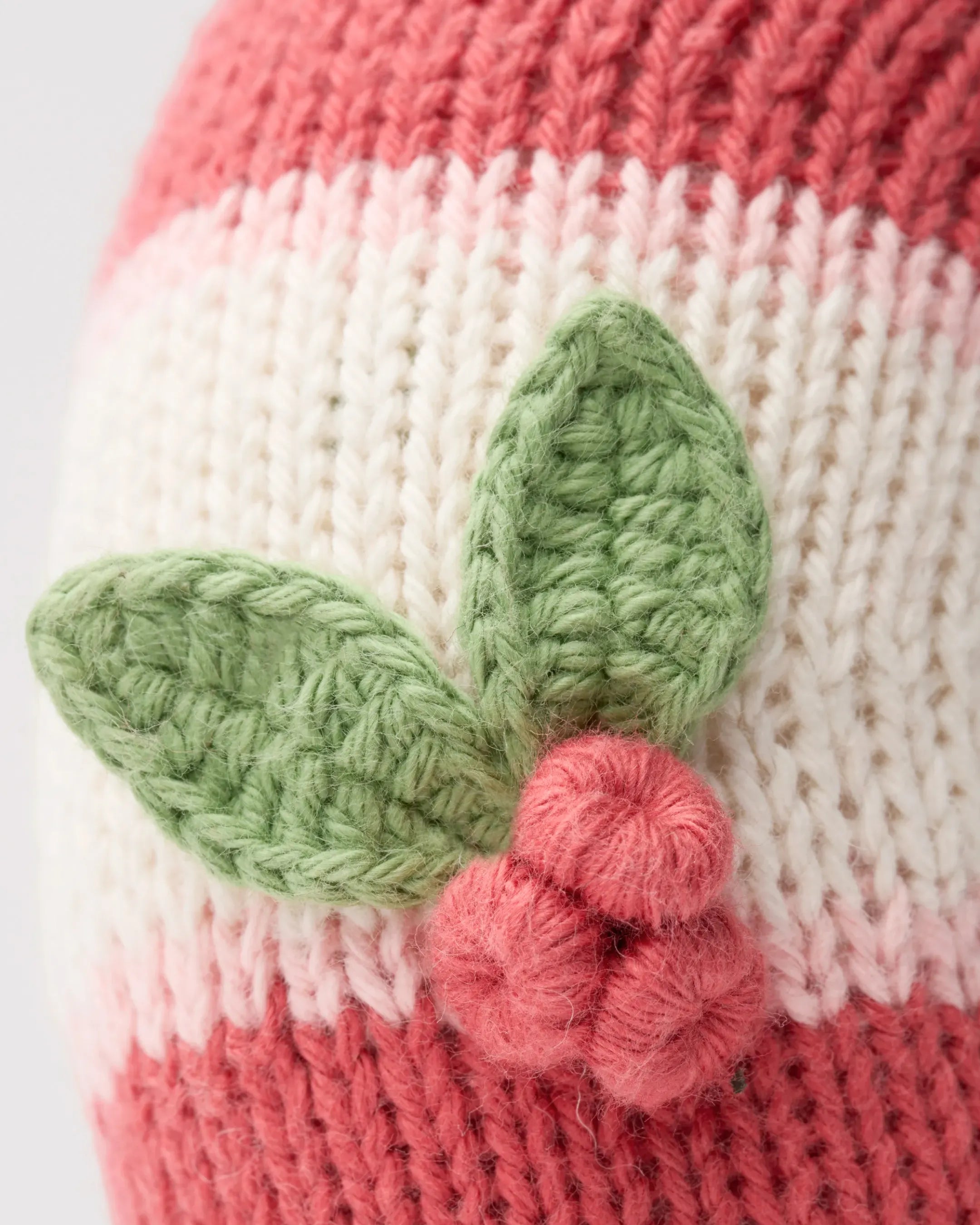 Close-up of knit holly leaves and a red berry on a candy cane