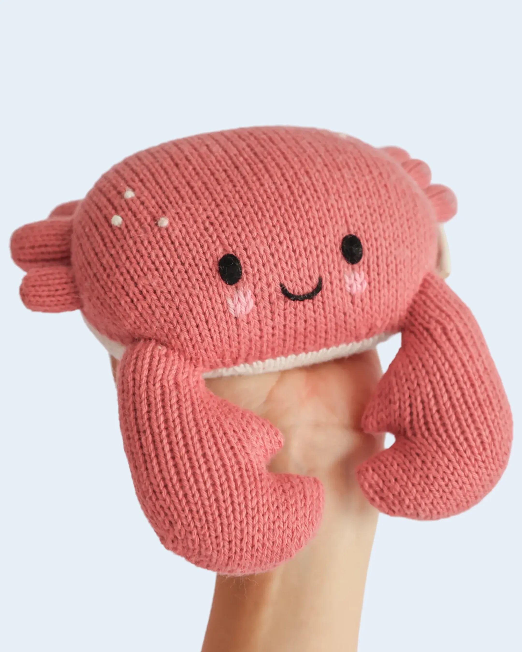 Hand-knit coral crab held in an open hand to show its small size