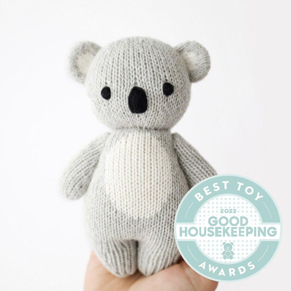 Hand-knit koala stuffed animal held in an open hand to show its small size