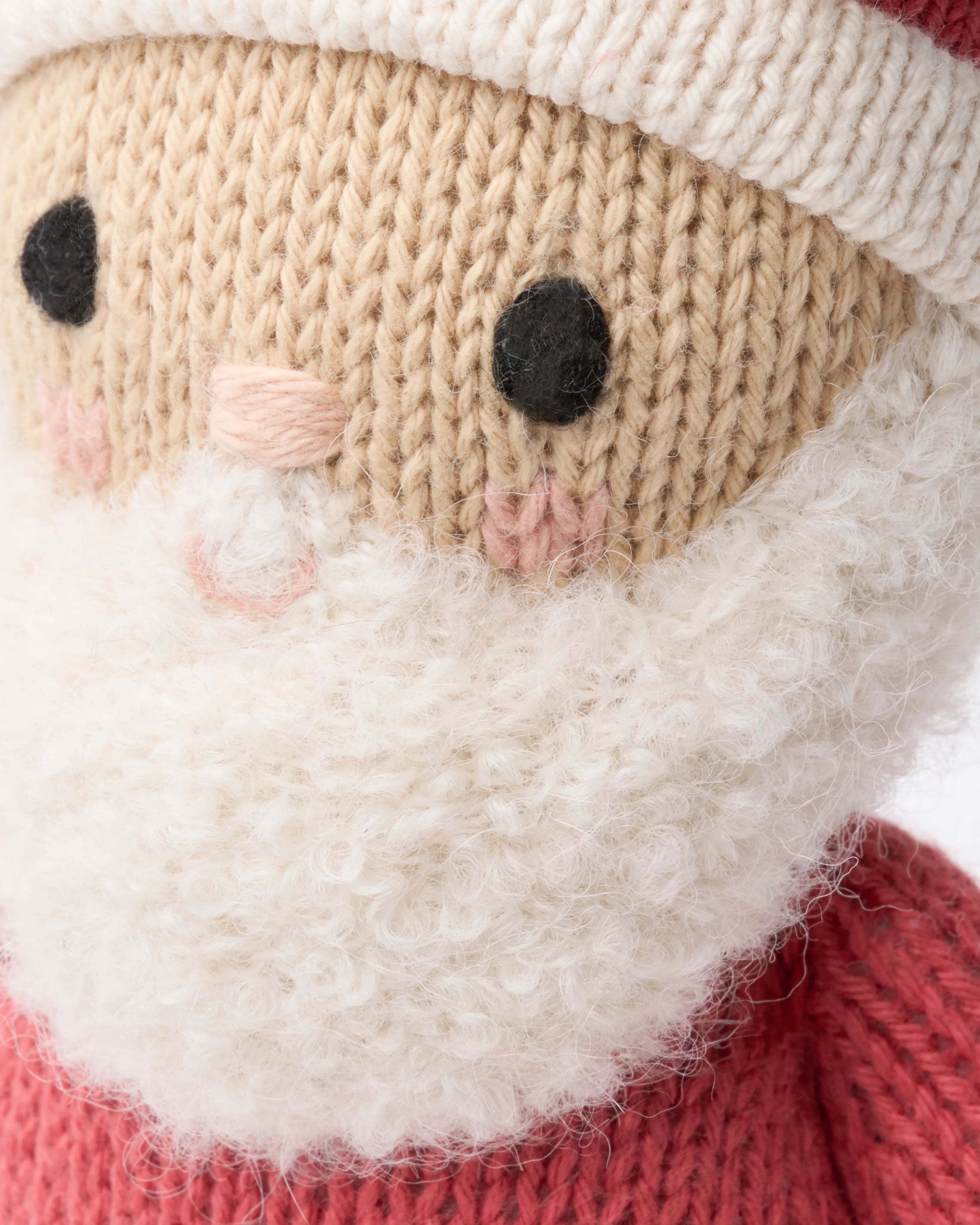 Close-up of a hand-knit Santa face with rosy cheeks and a fluffy white beard
