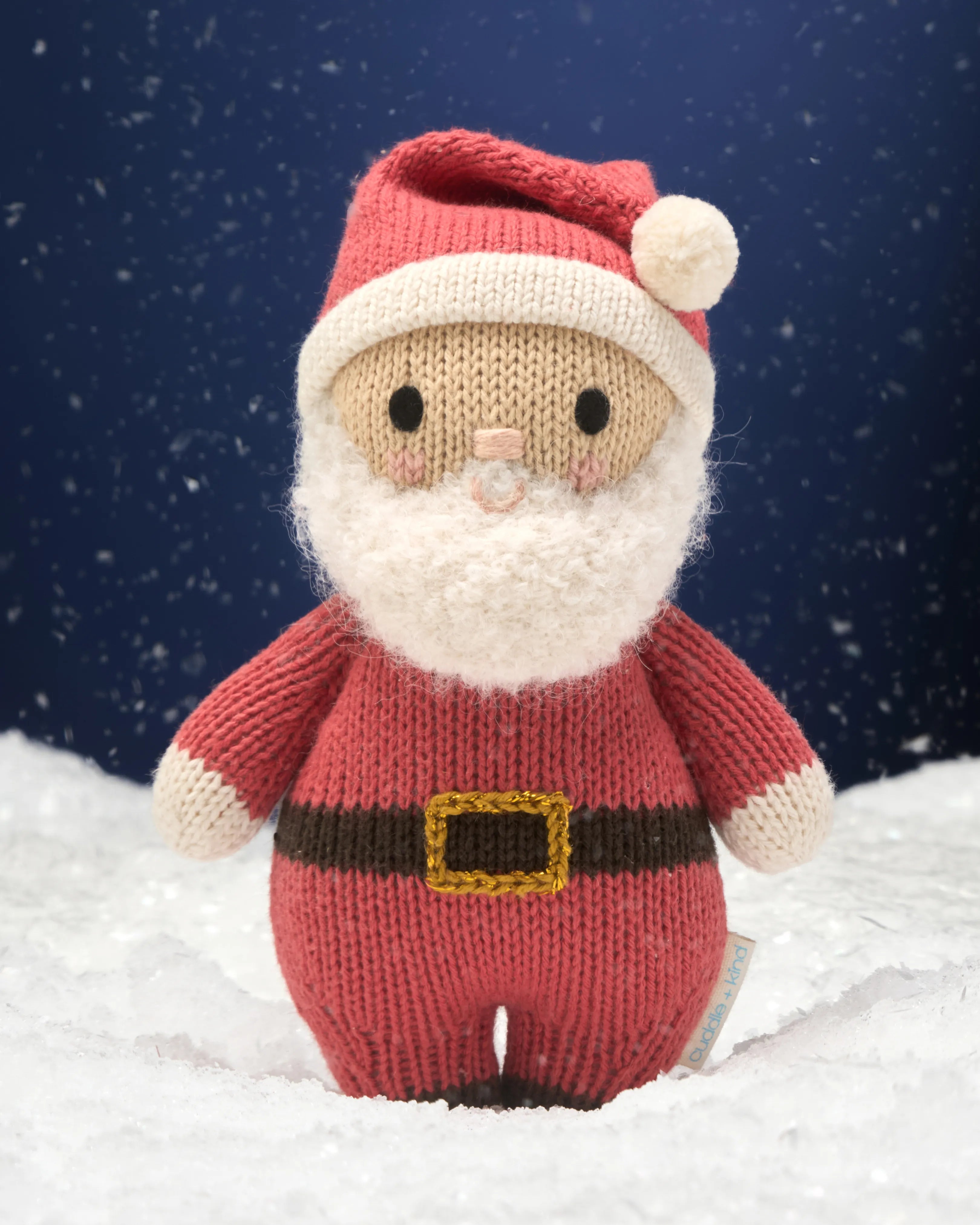 Hand-knit Santa doll standing in snow against a night sky