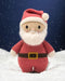 Hand-knit Santa doll standing in snow against a night sky