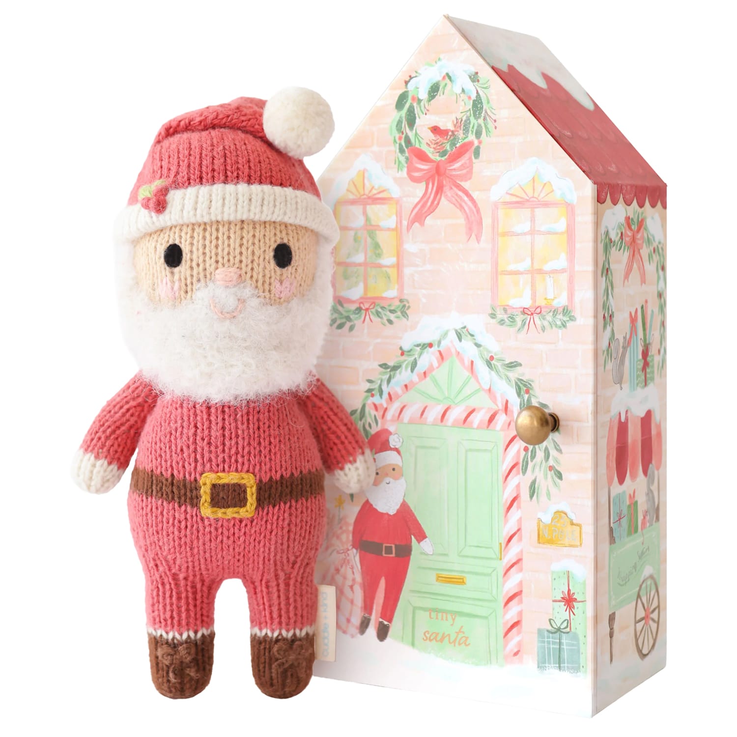 Small hand-knit Santa doll standing beside his illustrated house box