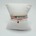 Four bracelets on a white pillow: gold beads, multicolor seed beads, pink seed beads and white seed beads with a red cross charm