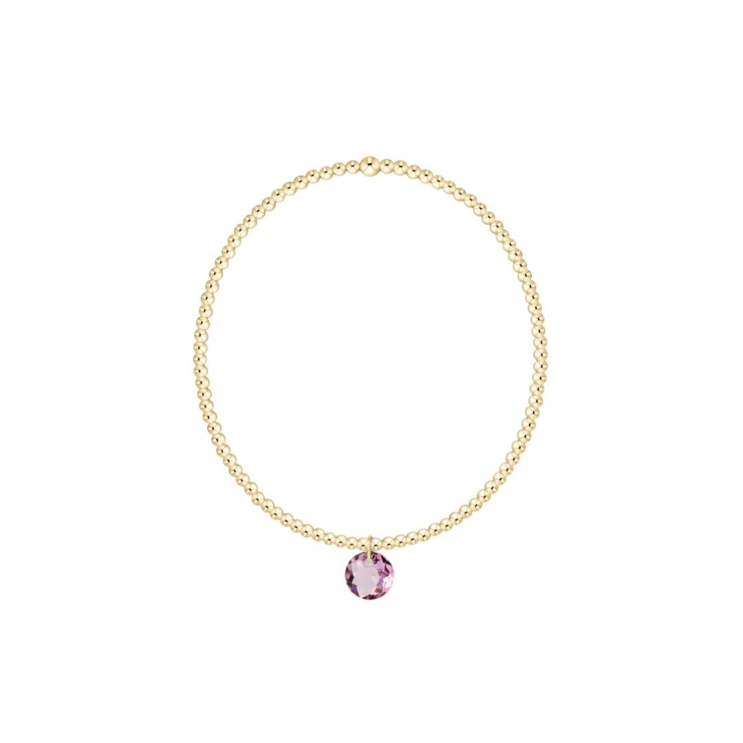 Gold bracelet with a pink pendant on a white background