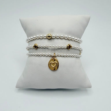 Three pearl bracelets on a white pillow with a gold bead, two gold crosses and a gold heart charm