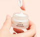 Hand holding an open jar of Eye'm Revived eye cream