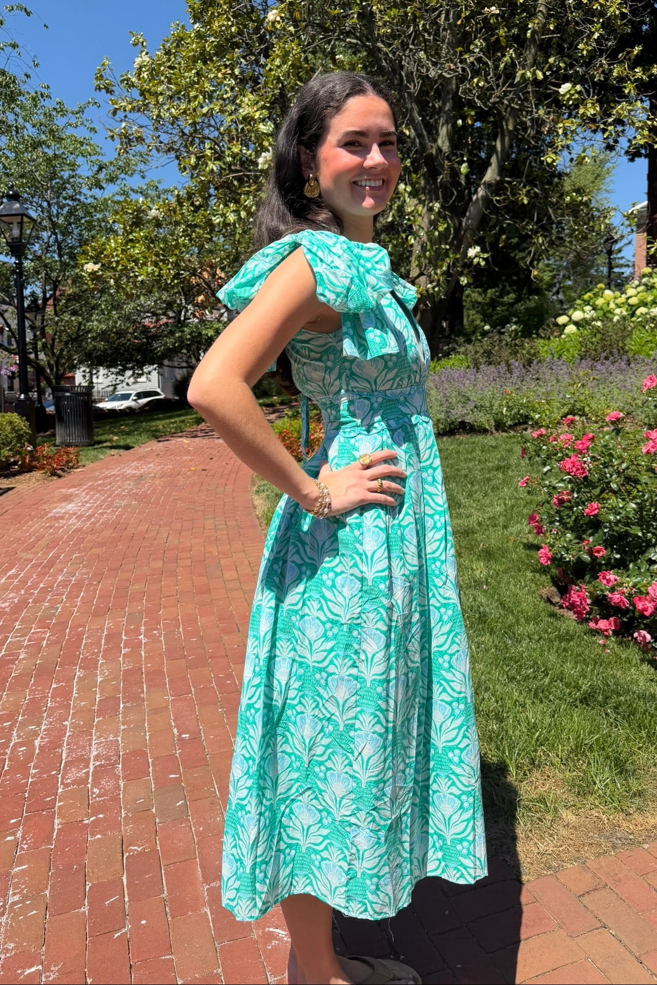 Woman in a green dress standing outdoors with trees and flowers in the background