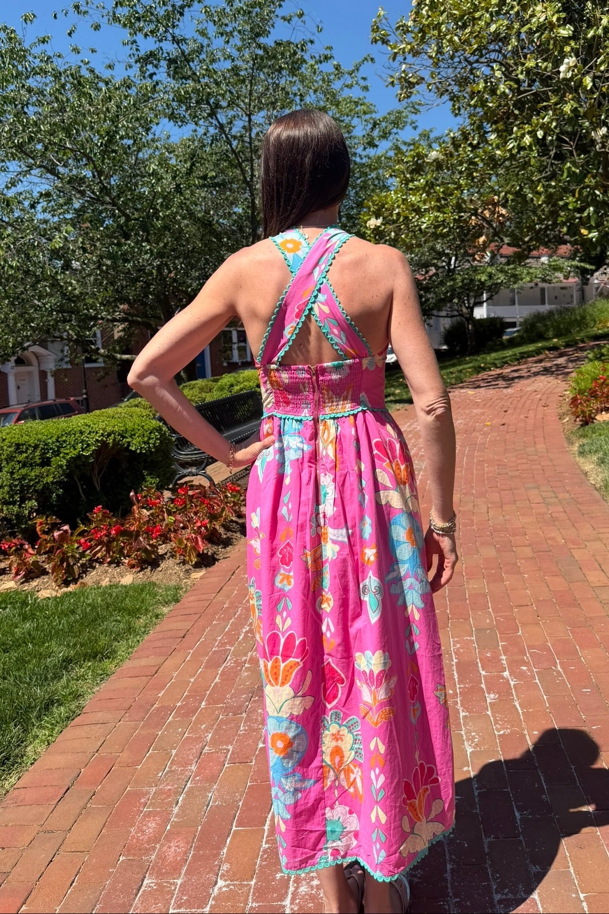 Woman in a colorful dress walking on a brick path with trees and greenery in the background