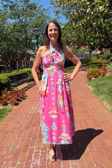 Woman in a pink floral dress standing on a brick path with trees and greenery in the background