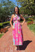 Woman in a pink floral dress standing on a brick path with trees and greenery in the background